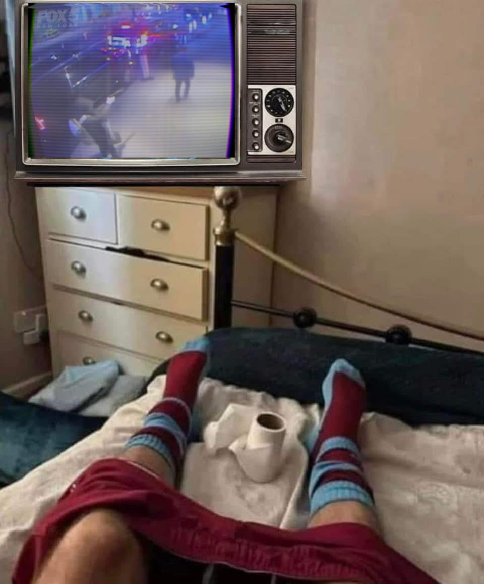 This meme is a screenshot of a person's legs and feet on a couch, wearing a Liverpool FC jersey and socks, with a TV in the background showing a Liverpool vs. Manchester United game. The image is captioned "When your team is winning but you're still in bed".